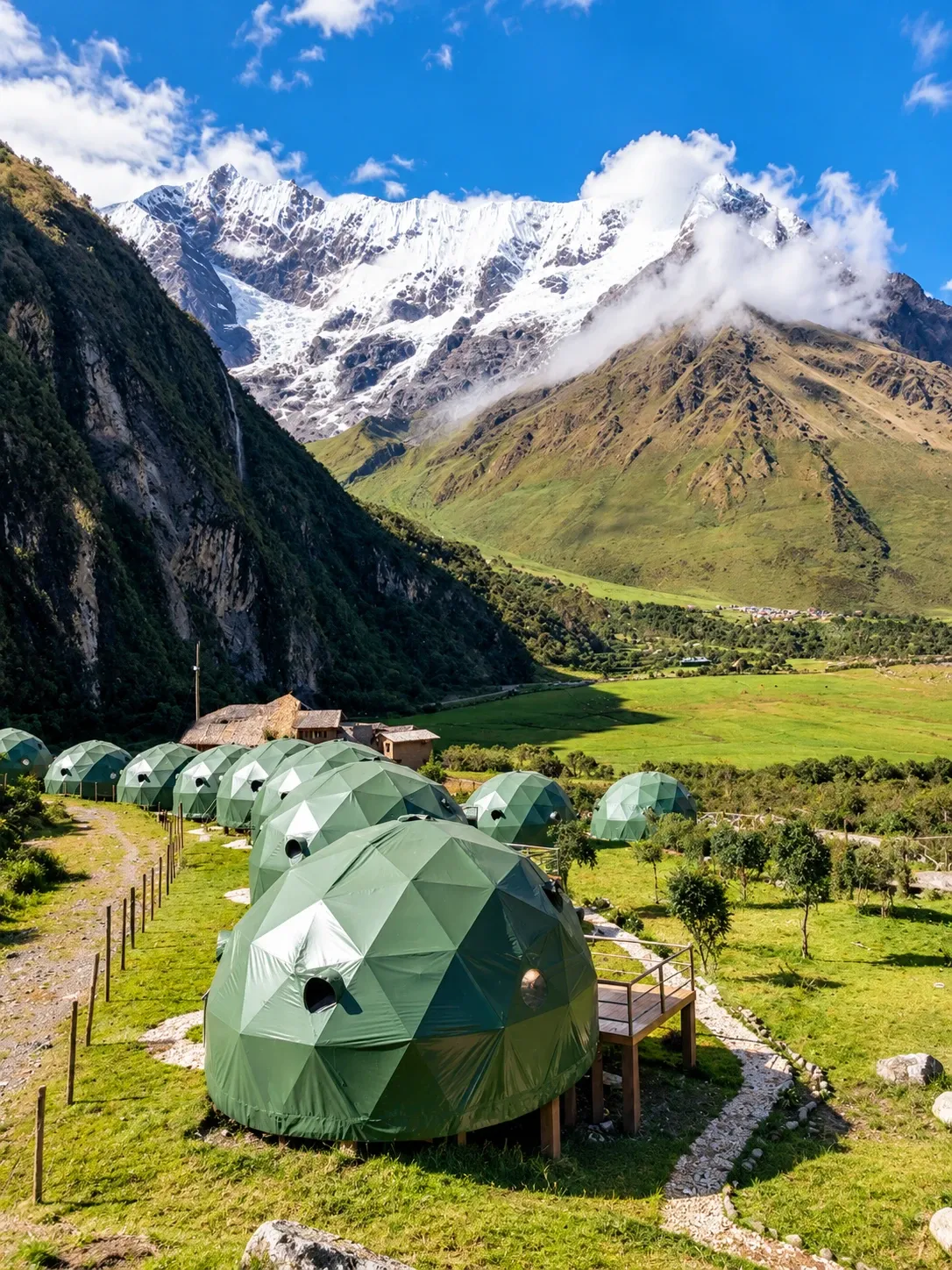 Glamping domes on the valley floor below a snow-covered peak
