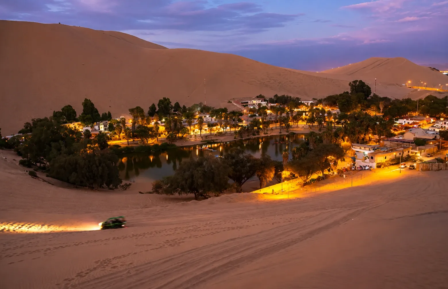The Huacachina oasis lit up among the dunes at dusk