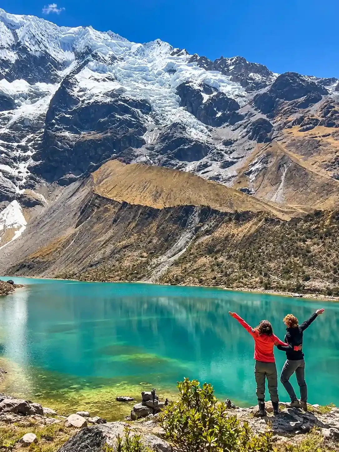 Two walkers above Humantay Lake with the glacier behind