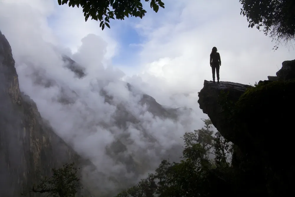 A walker silhouetted on a rock ledge above a cloud-filled gorge