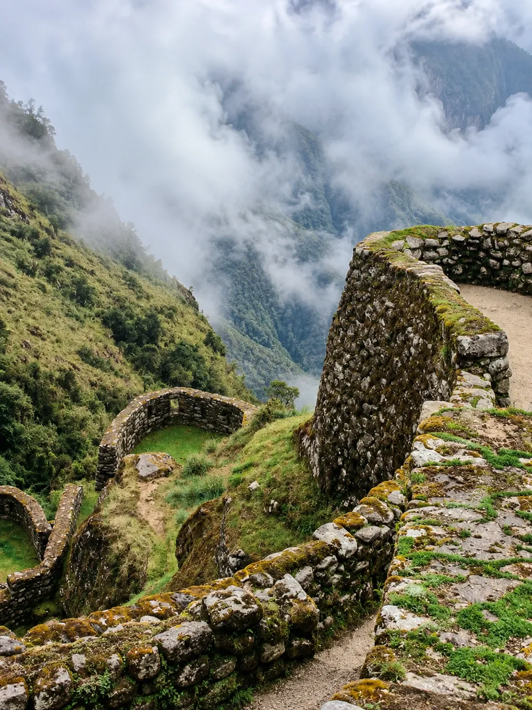 A curved Inca wall on the trail with cloud filling the valley below