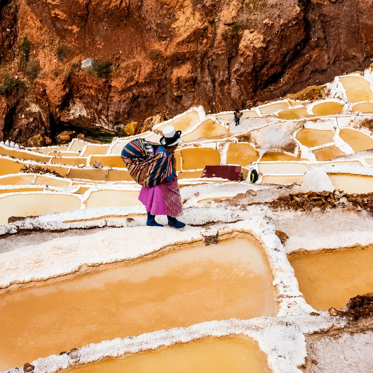 A woman carrying salt between the evaporation ponds at Maras
