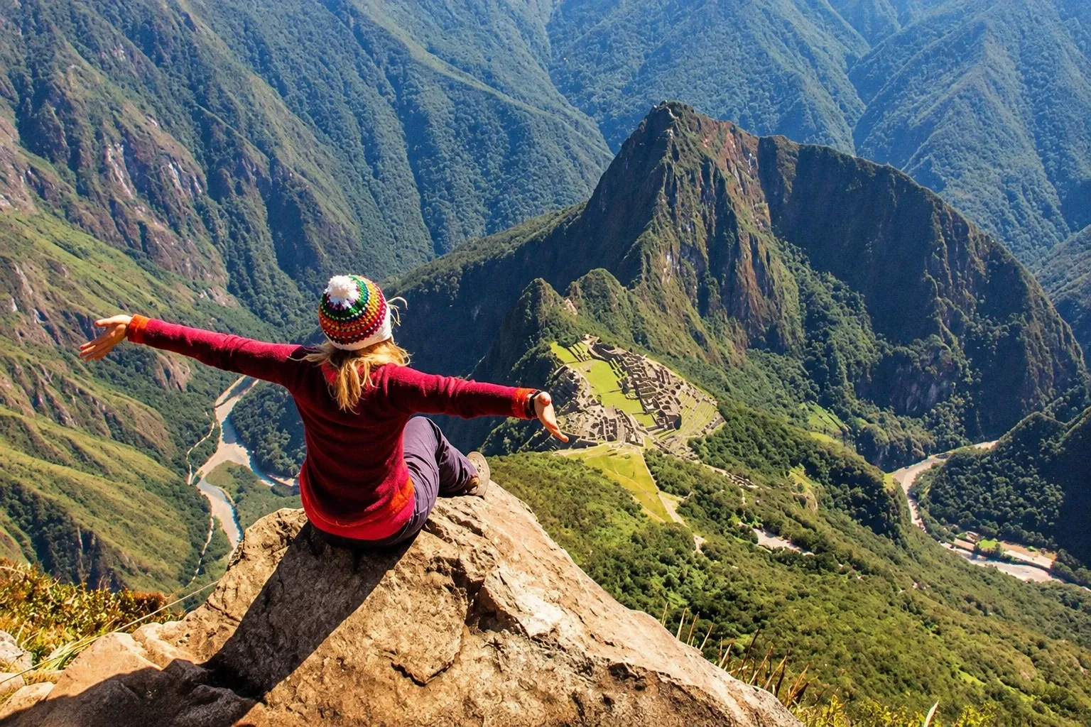 A walker sitting on the summit rocks of Huayna Picchu, the citadel far below