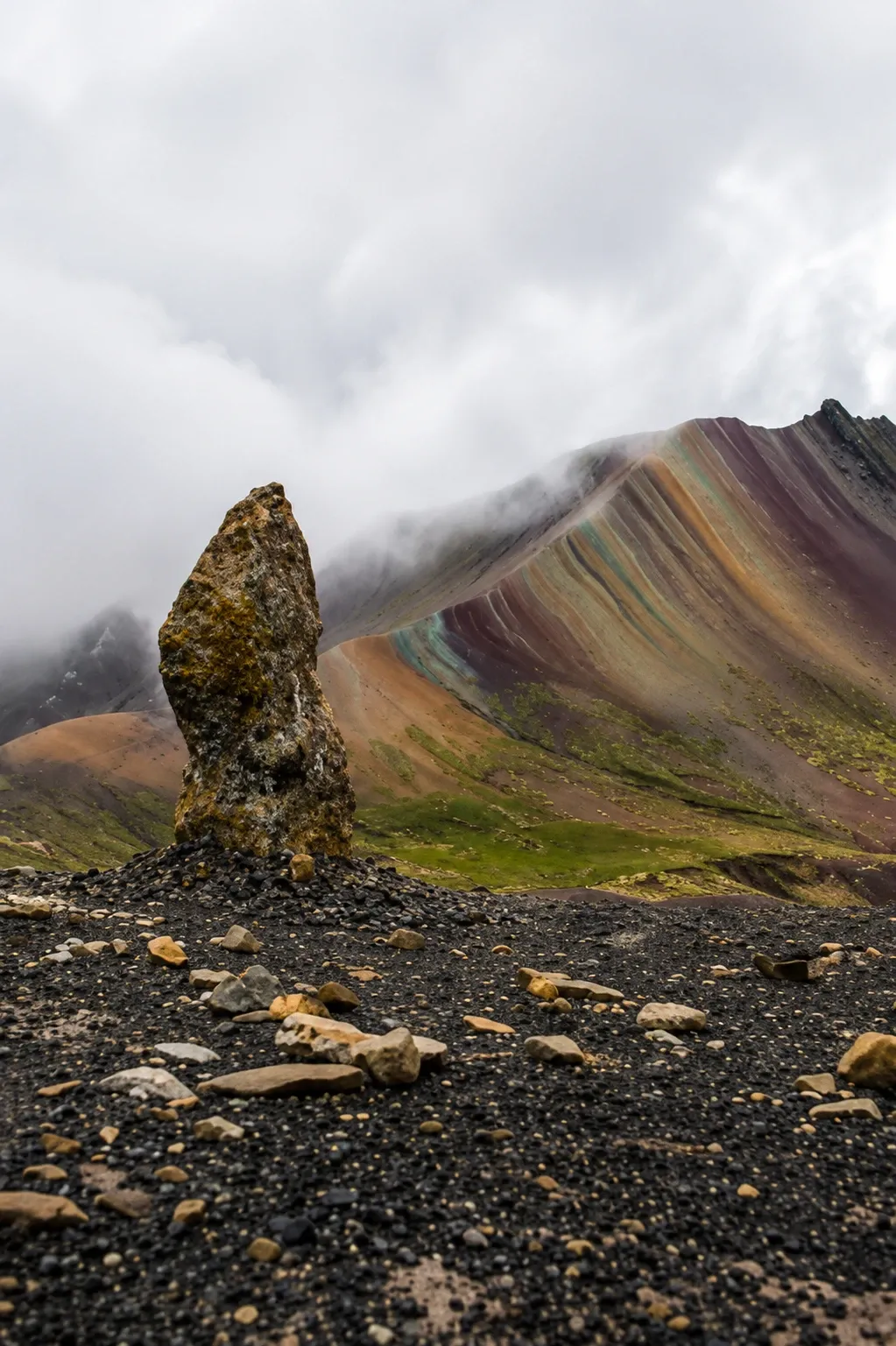 A standing rock at Palcoyo with coloured slopes behind it