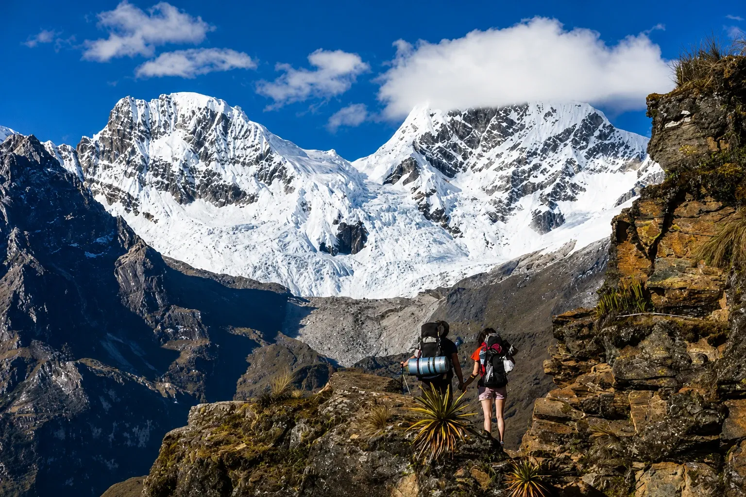 Walkers on a rocky ledge beneath the glaciers of Salkantay