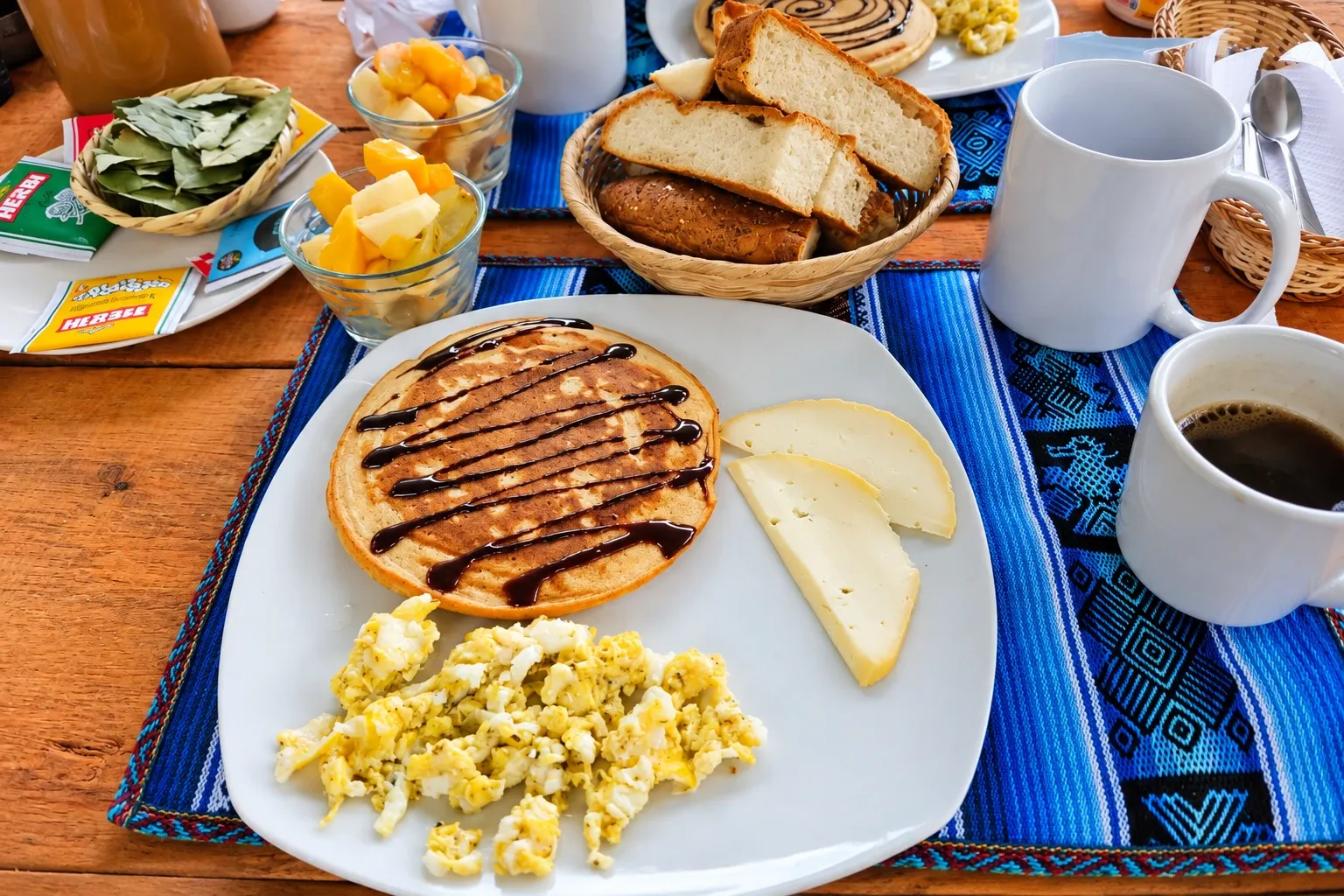Pancakes, eggs, bread and coffee on a woven tablecloth